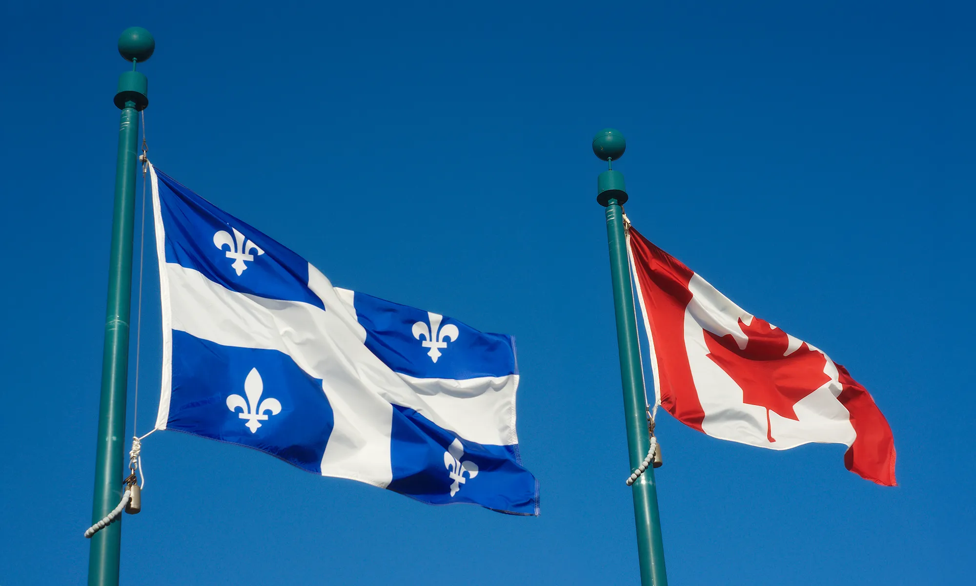 Drapeaux du Québec et du Canada flottant sous un ciel bleu, symbolisant l’importance du marketing local pour les entreprises du Québec.